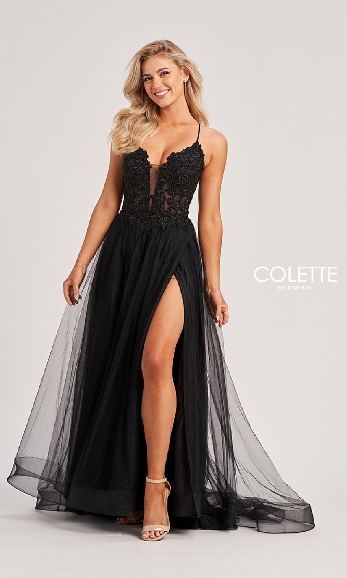 A woman poses against a plain background in the Long Prom Dress: Colette CL8320, a black, floor-length gown with an embroidered bodice, high slit, sheer skirt, spaghetti straps, and sleeveless design.